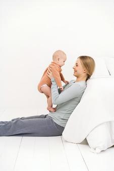枕に寄り掛かり足を伸ばし抱っこする女性 枕に寄り掛かり足を伸ばし抱っこする女性 親子,ベッド,寄り掛かるの写真素材