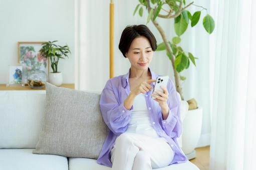 部屋でスマホを使うミドル女性 スマホ,笑顔,女性の写真素材