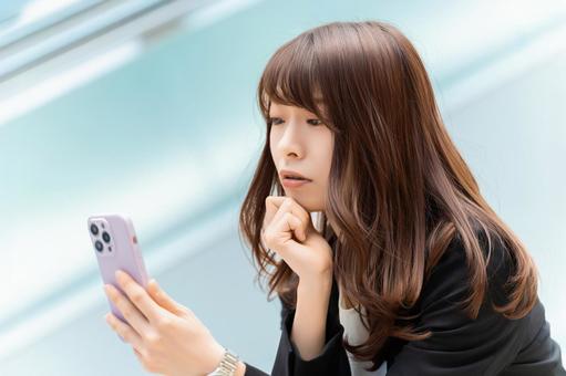 スマホを見て考える女性・ビジネスウーマン スマホを見て考える女性・ビジネスウーマン 女性,考える,スマホの写真素材