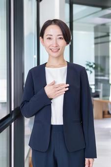 笑顔で胸に手を当てるスーツ姿の女性 ビジネス,女性,案内の写真素材