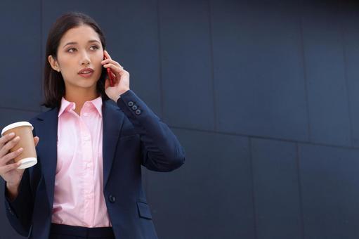 オフィスビルの外でコーヒー片手に電話するビジネスウーマン ビジネスウーマン,ビジネス,女性の写真素材