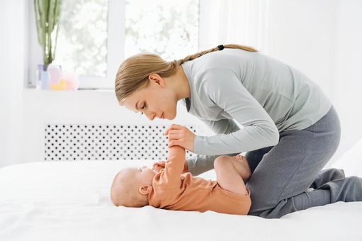 仰向けに寝かせた赤ちゃんの手を握り見つめる女性 仰向けに寝かせた赤ちゃんの手を握り見つめる女性 親子,横向き,横顔の写真素材