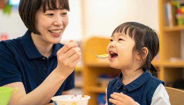 子どもにご飯をあげる保育士の写真