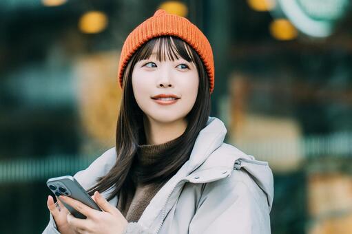 冬の街角でスマホを使う笑顔の女性 冬,女性,街の写真素材