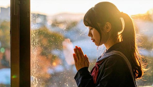 手を合わせて受験合格を祈る制服の女子高生の写真