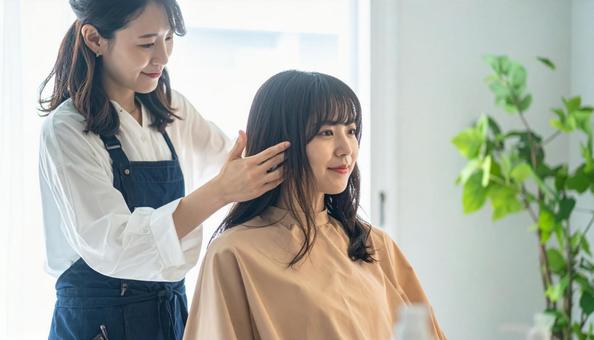 美容室の女性美容師が女性客の長い髪を触るの写真