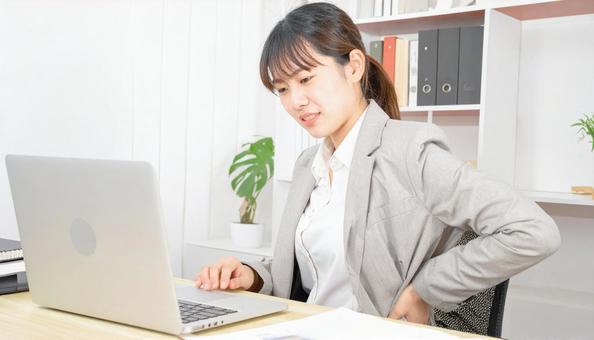 デスクワーク中に腰痛に悩むビジネスマンの写真