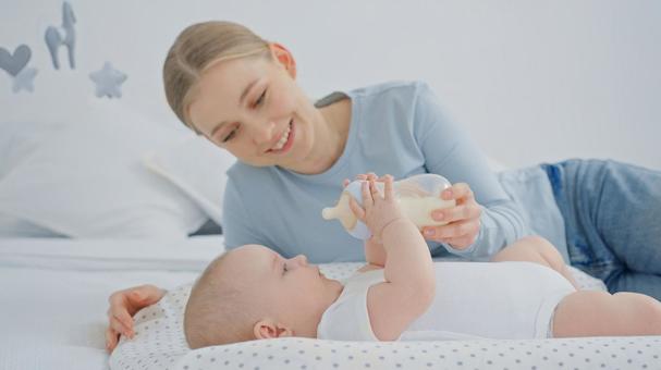 笑顔で赤ちゃんの持つ哺乳瓶を支える女性 笑顔で赤ちゃんの持つ哺乳瓶を支える女性 赤ちゃん,哺乳瓶,持つの写真素材