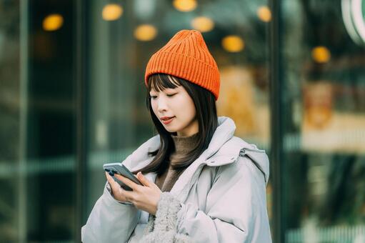 冬の街角でスマホを使う笑顔の女性 冬,女性,街の写真素材