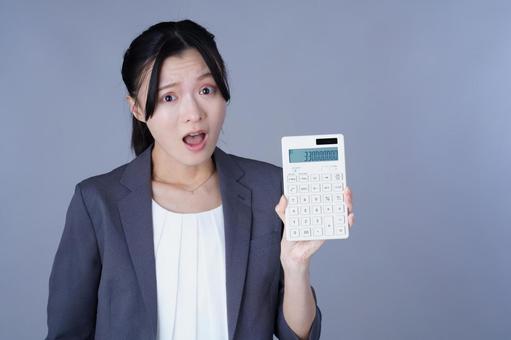 電卓を見せて驚いているスーツ姿の女性の写真