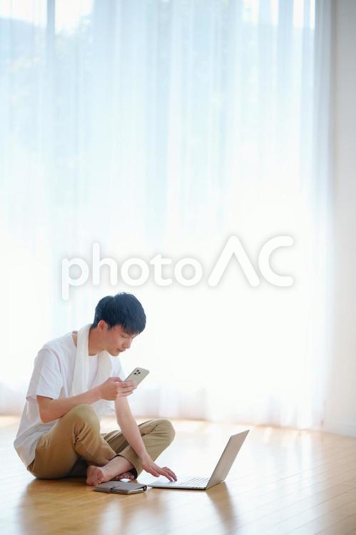 お風呂上がりに床に座ってノートパソコンとスマートフォンを使う男性 お風呂,お風呂上がり,男性の写真素材