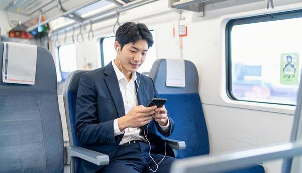 電車に座って携帯電話を見るビジネスマン 電車に座って携帯電話を見るビジネスマンの写真