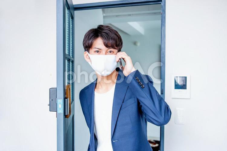 マスクをしてドアから電話して入ってくる男性 マスク,スマホ,コロナ対策の写真素材