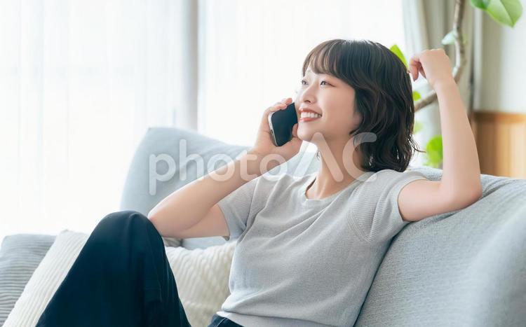 ソファに座ってスマホで話す笑顔の女性 女性,スマホ,スマートフォンの写真素材