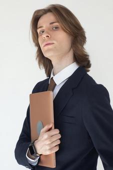 ノートパソコンを抱えるカメラ目線で顎を上げたスーツの男性 男性,外国人,欧米人の写真素材