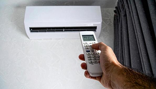クーラーにリモコンで設定ボタンを押す手の写真