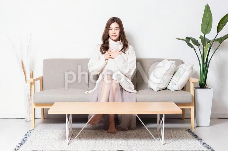 リビングのソファに座って、胸に手を当てる若い女性 女性,リビング,ソファの写真素材