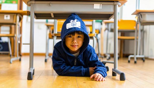 防災ずきんをかぶって机の下に隠れる男の子 防災ずきんをかぶって机の下に隠れる男の子の写真