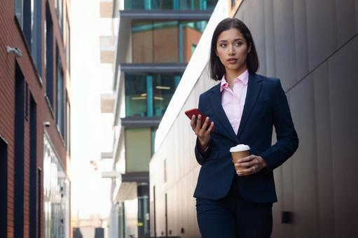 街なかでコーヒーとスマートフォンを持って立っているビジネスウーマン ビジネスウーマン,ビジネス,女性の写真素材