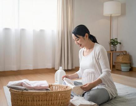 ベビー服を畳みながら微笑む妊婦の準備時間の写真