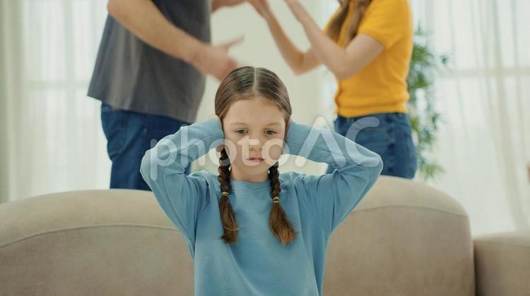 耳を塞ぐ女の子と後ろで喧嘩する両親 女の子,両親,家族の写真素材