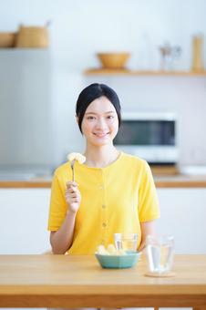 カメラ目線でフォークに刺したリンゴを持つ黒髪女性の写真