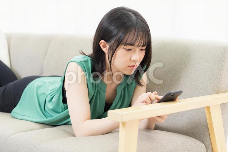 ソファに寝転んでスマホを使う若い女性 スマホ,若い,女性の写真素材