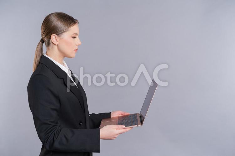 ノートパソコンを持ち立つ横向き女性 女性,横向き,横顔の写真素材