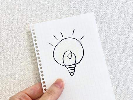 豆電球の絵が描かれた用紙を持つ手元 豆電球の絵が描かれた用紙を持つ手元 豆電球,アイデア,ポイントの写真素材