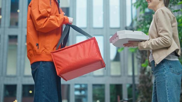 屋外でピザのデリバリーを受け取った女性と保温ピザバッグをもつフードデリバリー 配達,フードデリバリー,デリバリーの写真素材