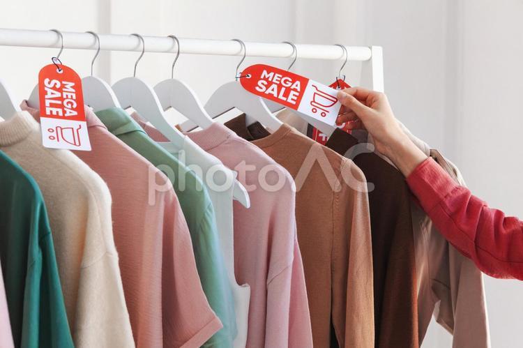 ハンガーに掛かった洋服のセールタグを触る女性の手元 セール,ショップ,女性の写真素材