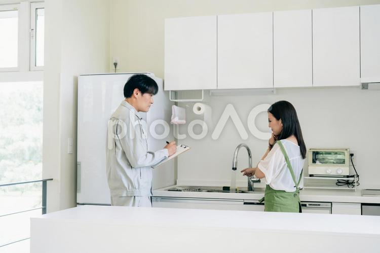 キッチンで話す作業着姿の男性と女性（水道・クレーム） 水道屋,水漏れ,苦情の写真素材