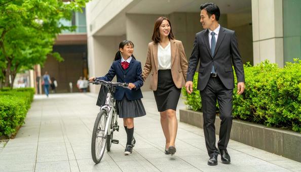 自転車を押して歩く制服の子供と共働き両親の写真