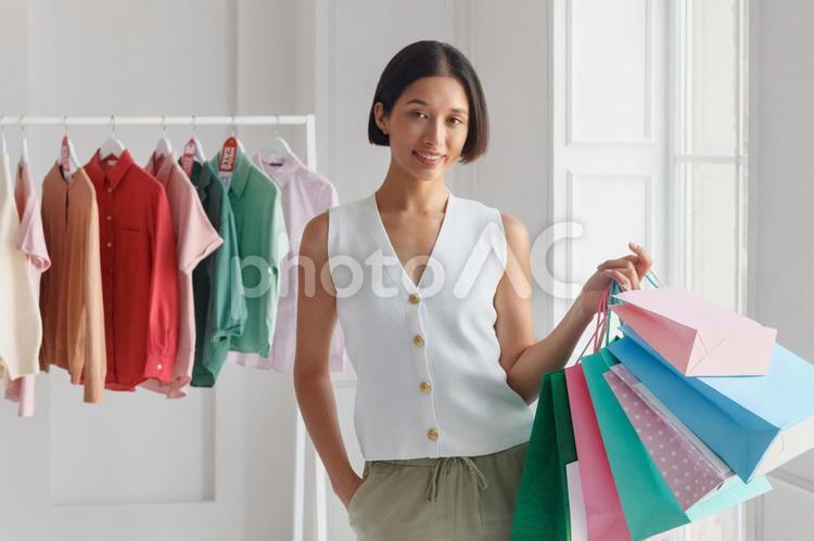 屋内でセールのタグの付いた洋服のハンガーラックの前で紙袋を持つアジア人女性 セール,ショップ,女性の写真素材