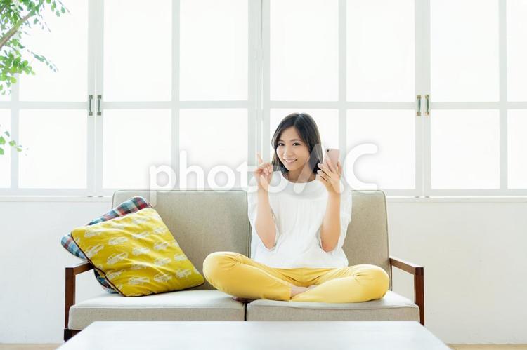 リビングでスマホを操作する若い女性 スマホ,若い女性,笑顔の写真素材