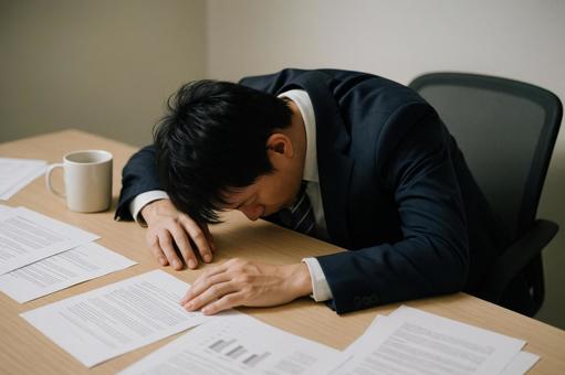 机に伏せる疲弊した部下の写真