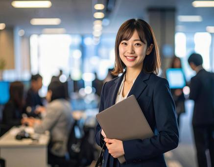 オフィスでPCを持って微笑む女性社員 オフィスでPCを持って微笑む女性社員の写真