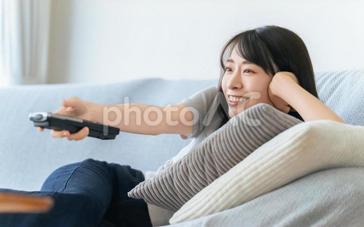 ソファに寝転んでテレビを見る女性 女性,テレビ,ソファの写真素材