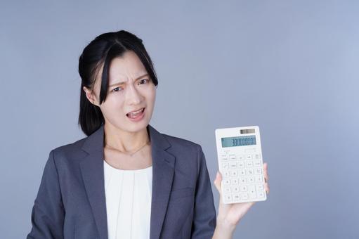 電卓を見せてしかめっ面のスーツ姿の女性の写真