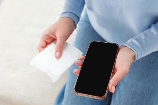 生理用ナプキンとスマートフォンを持っている女性 生理,月経,女性の写真素材