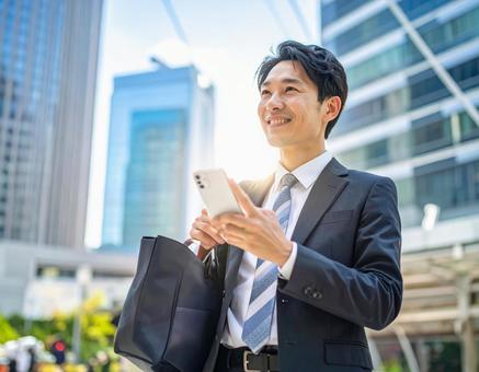 オフィス街でスマホを操作するサラリーマン オフィス街でスマホを操作するサラリーマンの写真