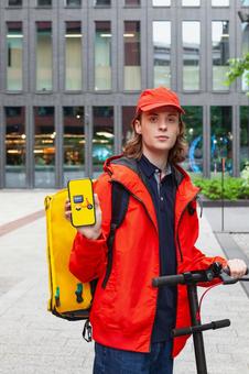 街なかでスマートフォンのアプリ画面を見せるフードデリバリーの男性 配達,フードデリバリー,デリバリーの写真素材