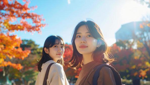 紅葉を背景に振り返る2人の若い女性の写真