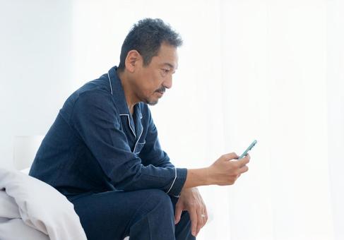 寝室でスマホを見るミドルの男性 寝室でスマホを見るミドルの男性 男性,スマホ,ミドルの写真素材