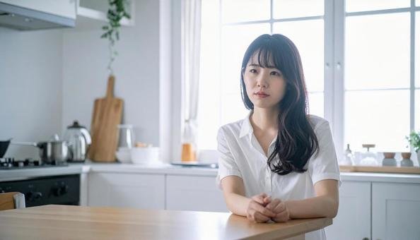 疲れた表情でキッチンに座る若い女性の写真