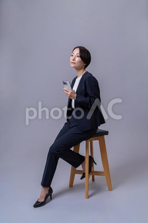 椅子に座り携帯を持つスーツを着た女性 ビジネスウーマン,転職,営業の写真素材