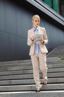 オフィスビルの外の階段を降りながらタブレットを見ているビジネスウーマン ビジネスウーマン,ビジネス,女性の写真素材