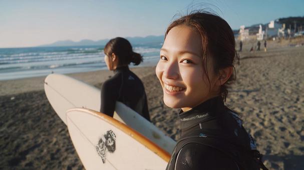 海辺の砂浜でサーフボードを抱え歩く女性 海辺の砂浜でサーフボードを抱え歩く女性の写真