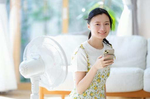 扇風機の横でスマホを持つ笑顔の女性 女性,スマートフォン,持つの写真素材