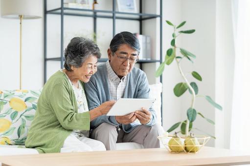 リビングでタブレットを見るシニアの夫婦 リビングでタブレットを見るシニアの夫婦の写真